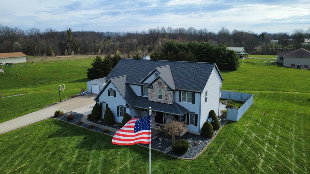 Aerial drone photo of a completed dark shingle roof on a Northeast Ohio home flying an American flag, by Firestone Roofing & Restoration.