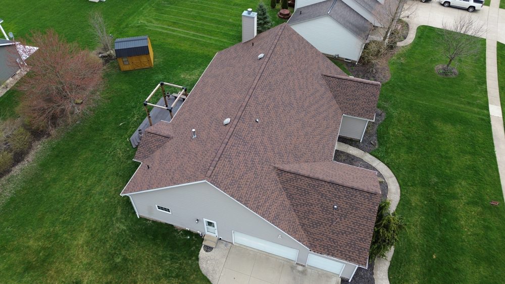 Drone photo of a completed brown shingle roof on a brick Northeast Ohio home framed by mature trees — Firestone Roofing & Restoration.