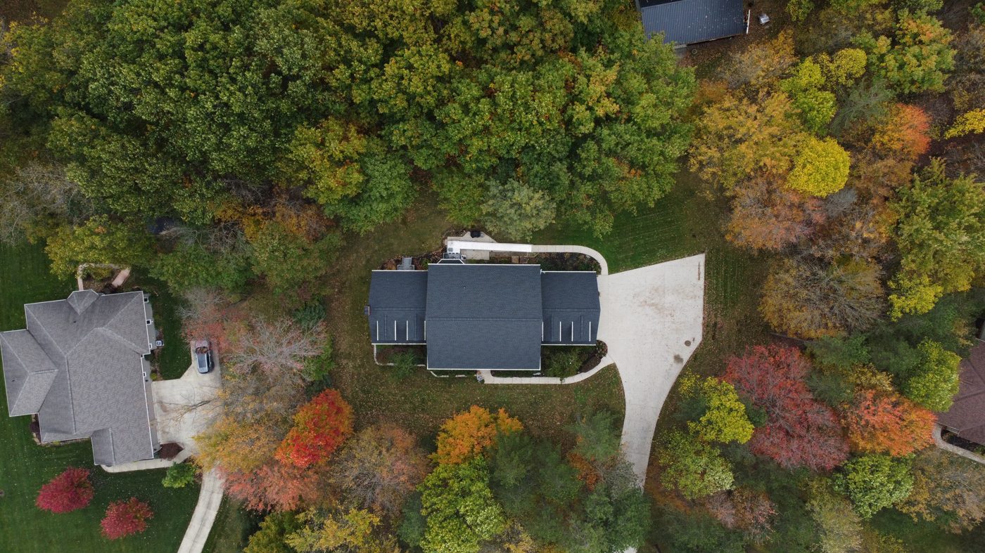Top-down aerial drone photo of a completed shingle roof framed by autumn trees in Northeast Ohio